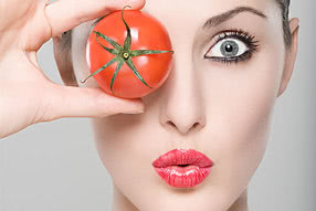 Frau verdeckt ein Auge mit Tomatenfrucht